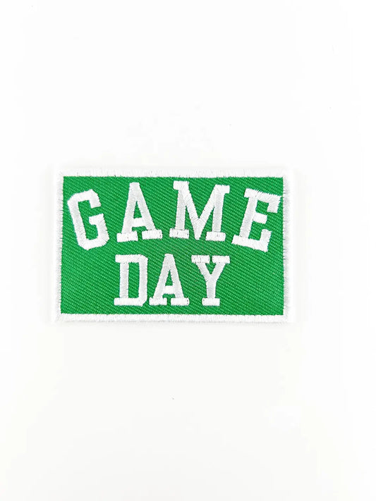 A rectangular embroidered patch with a green background and white border, featuring the words 'GAME DAY' in white varsity-style lettering, shown on a plain white background.
