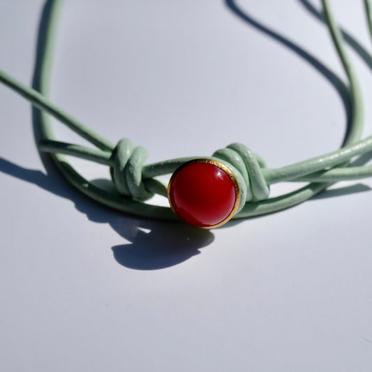 Green leather cord with a red coral stone on a light gray background