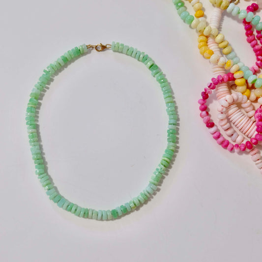 Green opal candy necklace layered with other colorful necklaces on a white background.