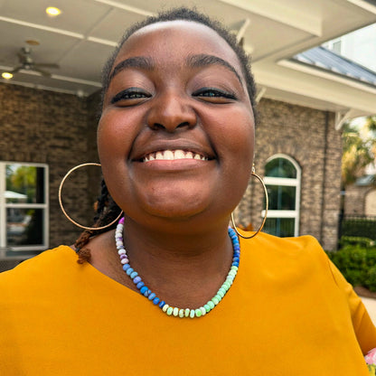 A student smiling and wearing a colorful custom gemstone candy necklace from a Key West DIY jewelry class.