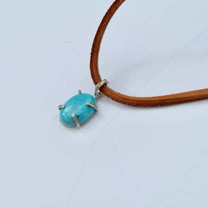 Kingman turquoise pendant on a brown suede cord against a light gray background