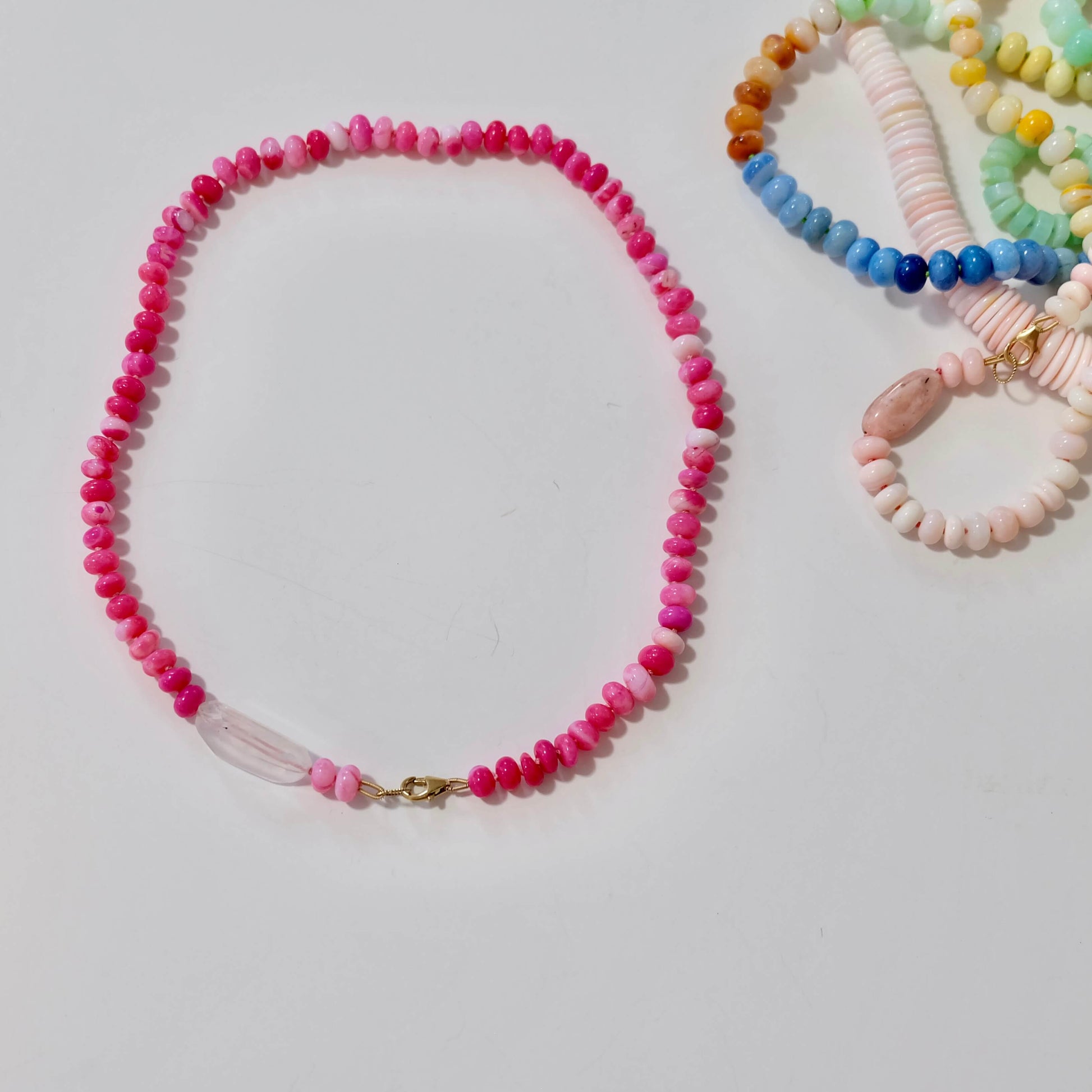 Layered hot pink candy necklace beads with pink beads and a bracelet with colorful beads on a light gray background