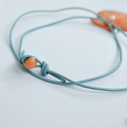 Light blue leather cord with a pink bead on a light gray background.