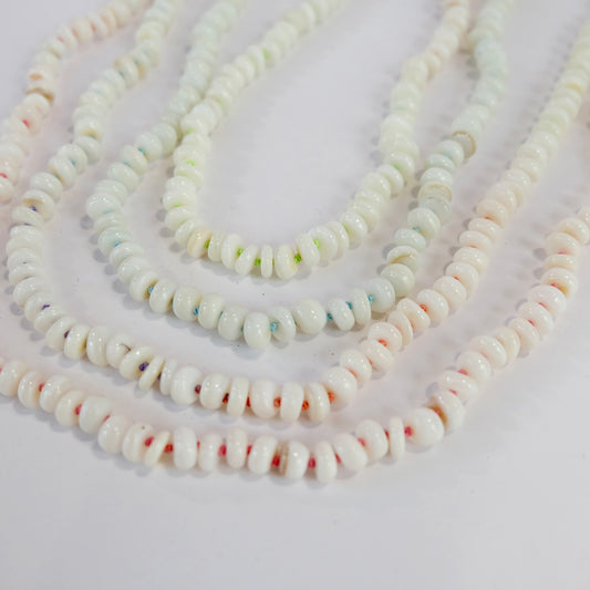 Collection of mother of pearl bead necklaces laying on flat surface.