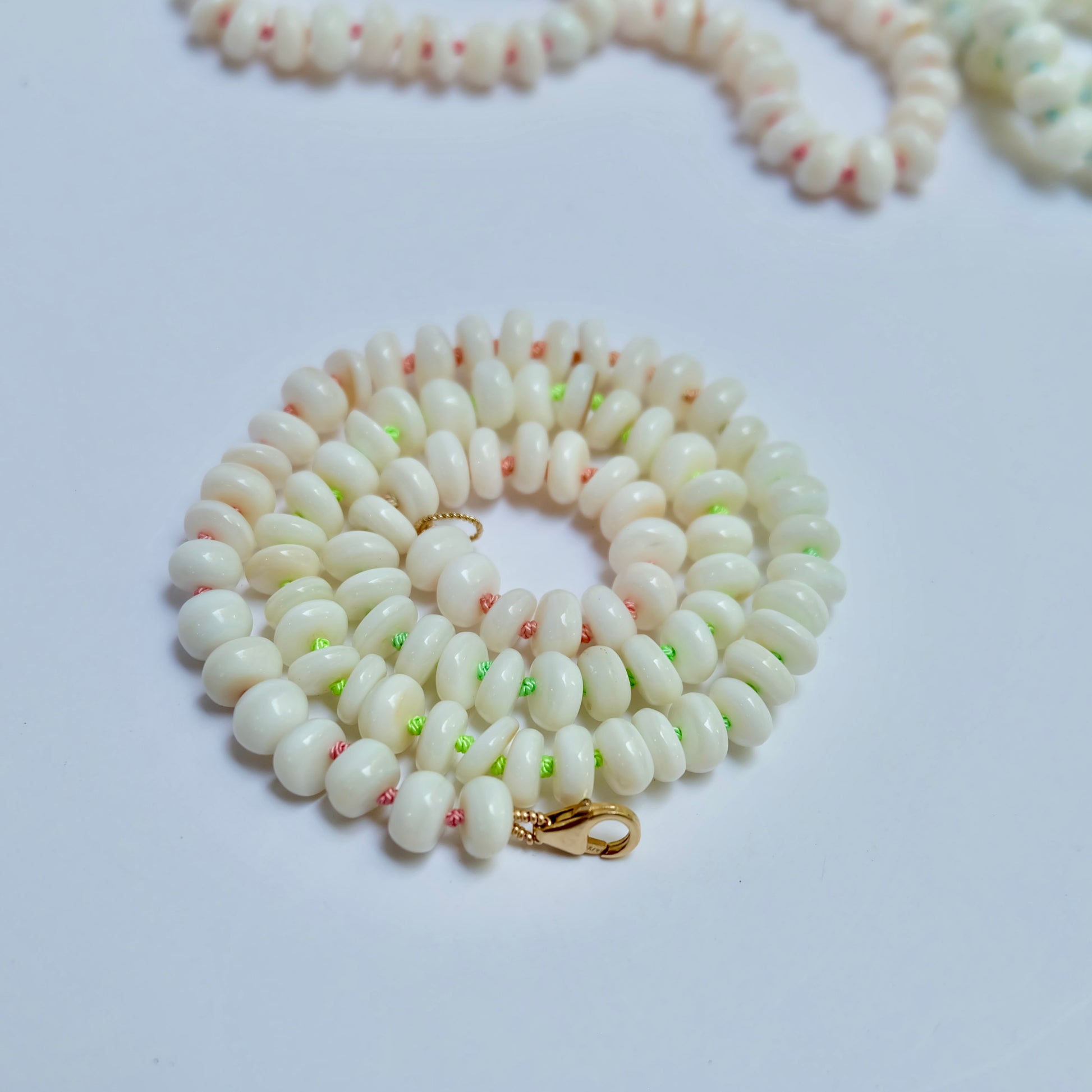 Mother of pearl necklace hand-knotted with pink and green silk lying in a swirl.