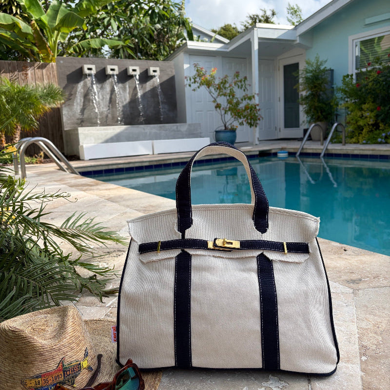 Navy blue Boatkin tote by a pool with a house and palm trees in the background.