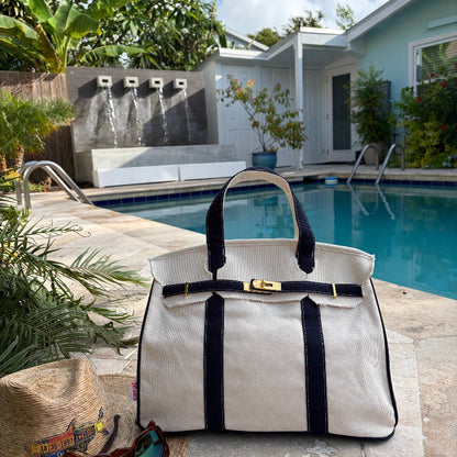 Navy blue Boatkin tote by a pool with a house and palm trees in the background.