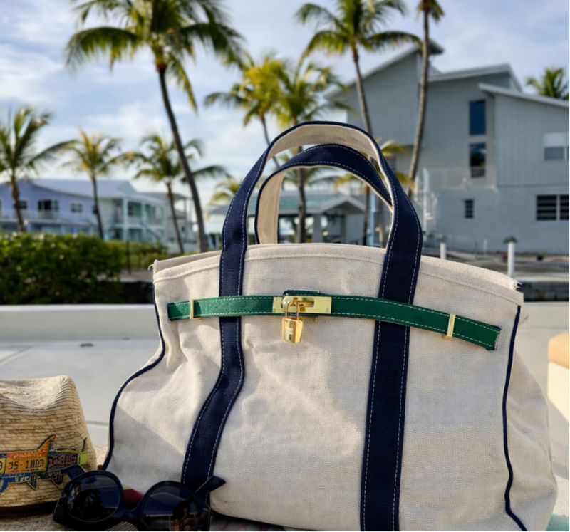 Navy and green Boatkin bag on a boat with palm trees and houses in the background.