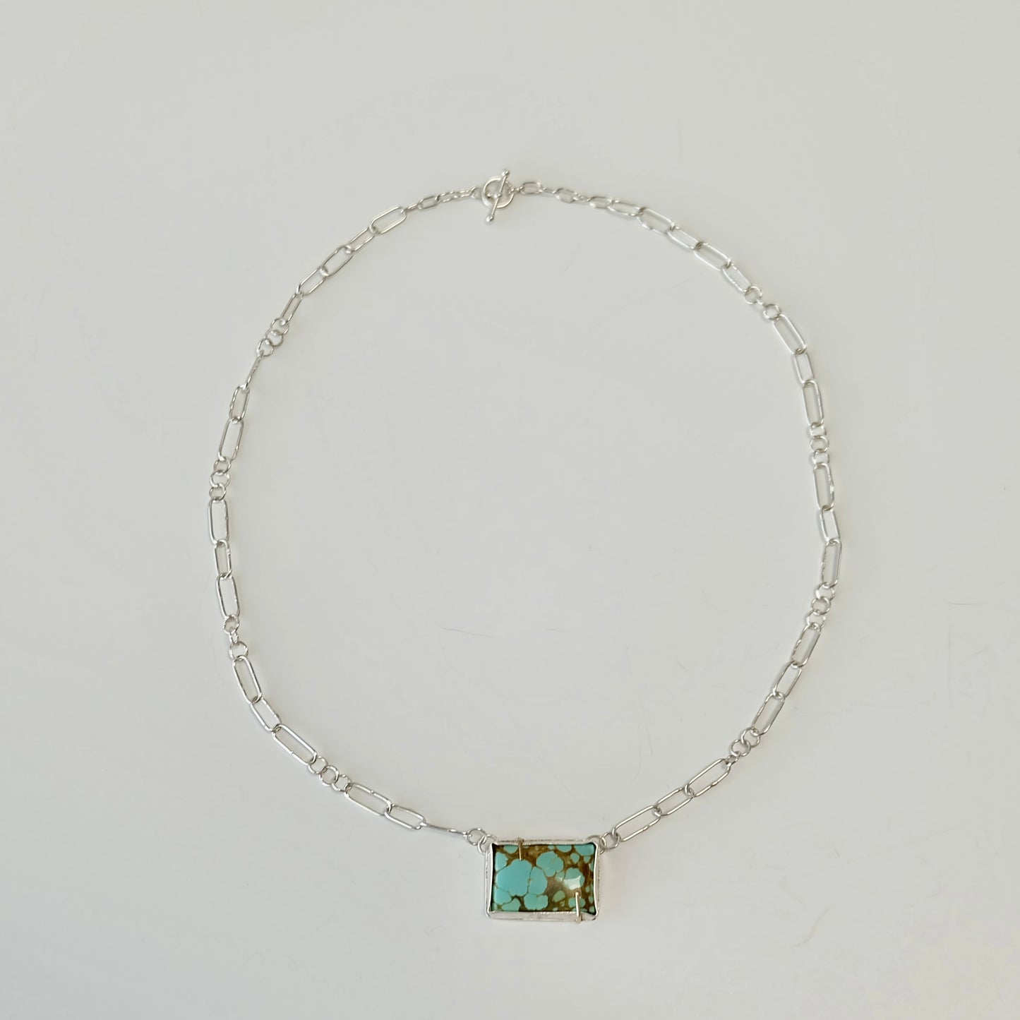 Silver necklace with a rectangular turquoise stone on a light gray background