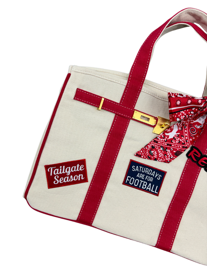 Detailed view of the left side of the Ole Miss canvas weekender tote bag showcasing embroidered Tailgate Season and Saturdays Are For Football iron on patches on beige canvas with red trim.