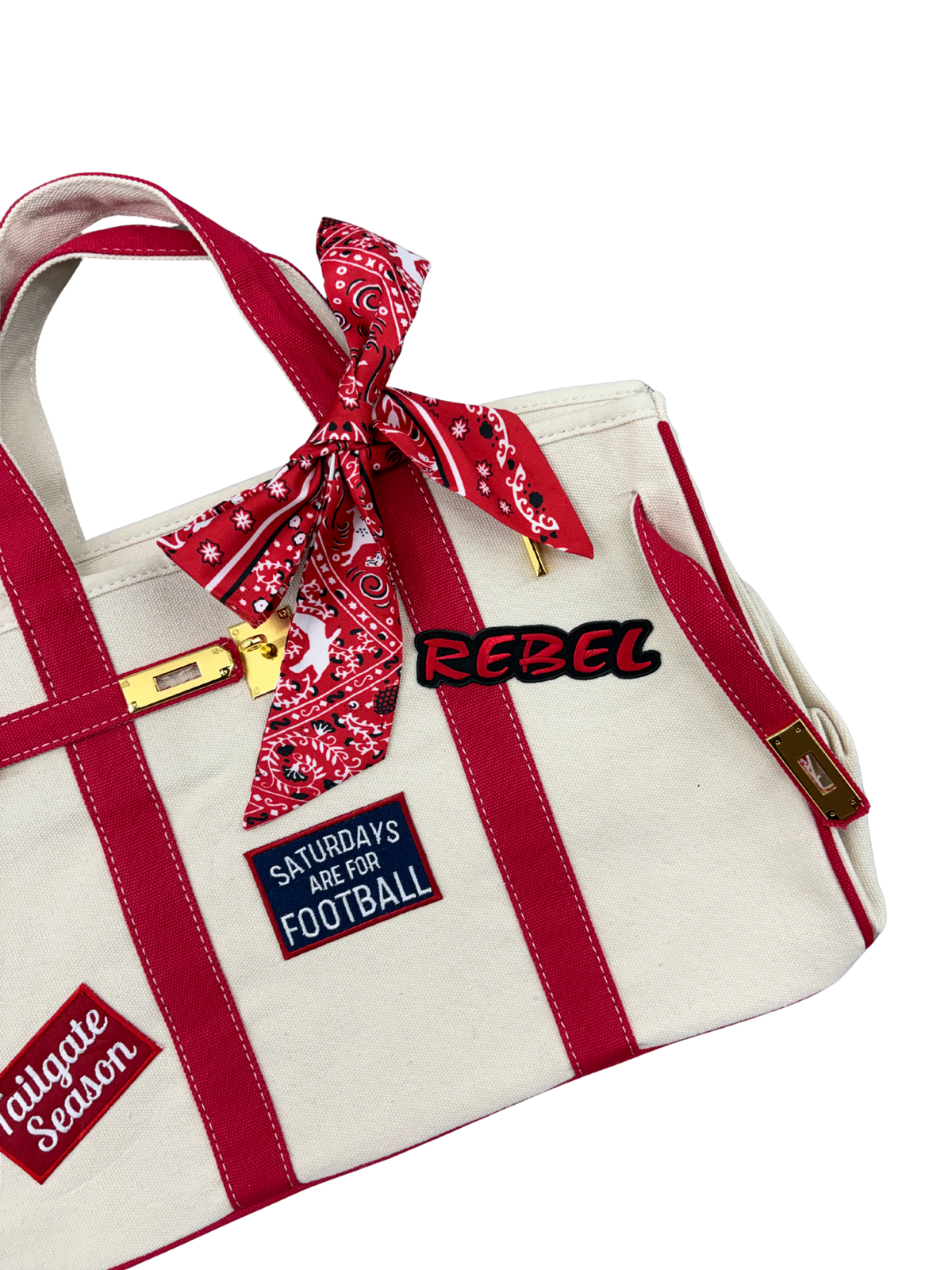 lose up view of Ole Miss college football tote bag in beige canvas with red structural piping, featuring an iron on Rebel patch and a red paisley twilly scarf tied to the handle.