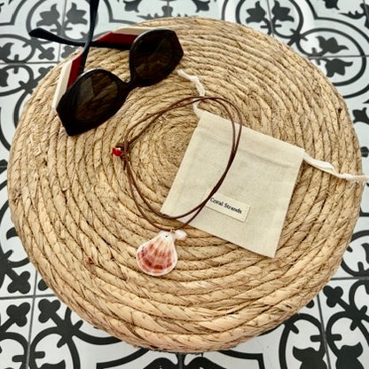 Peach fan shell pendant necklace with pearl on brown leather cord, styled on woven mat