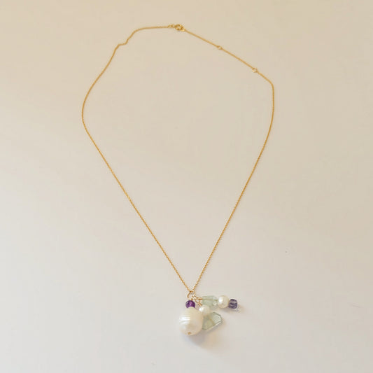 Close-up of baroque pearl, amethyst, and aquamarine charms on a dainty gold-filled necklace