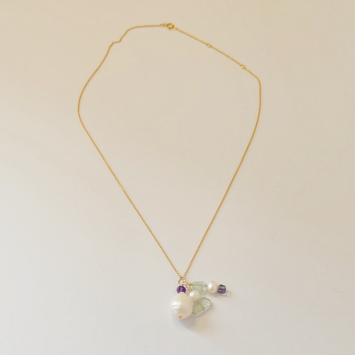 Close-up of baroque pearl, amethyst, and aquamarine charms on a dainty gold-filled necklace