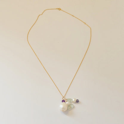 Close-up of baroque pearl, amethyst, and aquamarine charms on a dainty gold-filled necklace