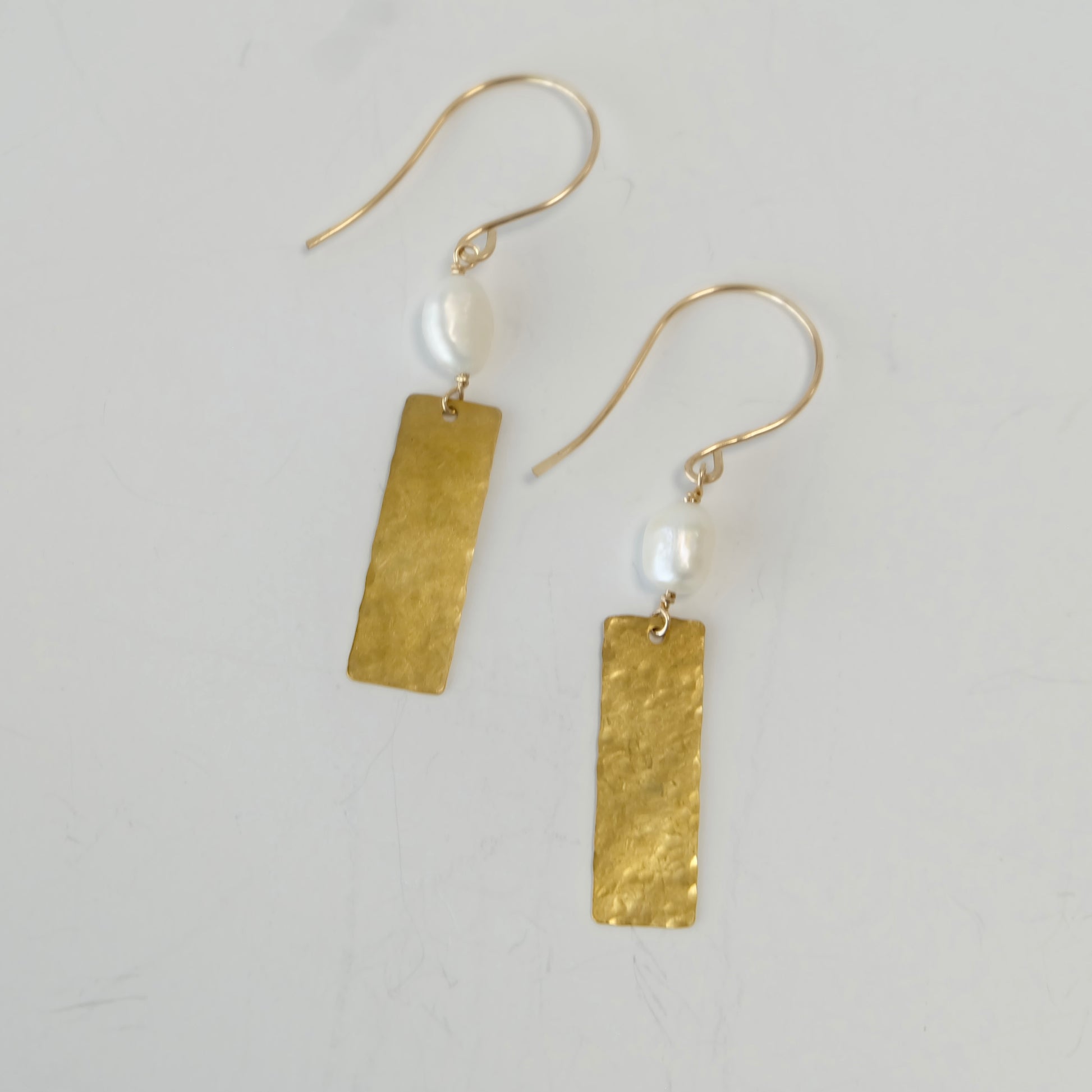 Pearl brass dangle earrings displayed on a light gray background
