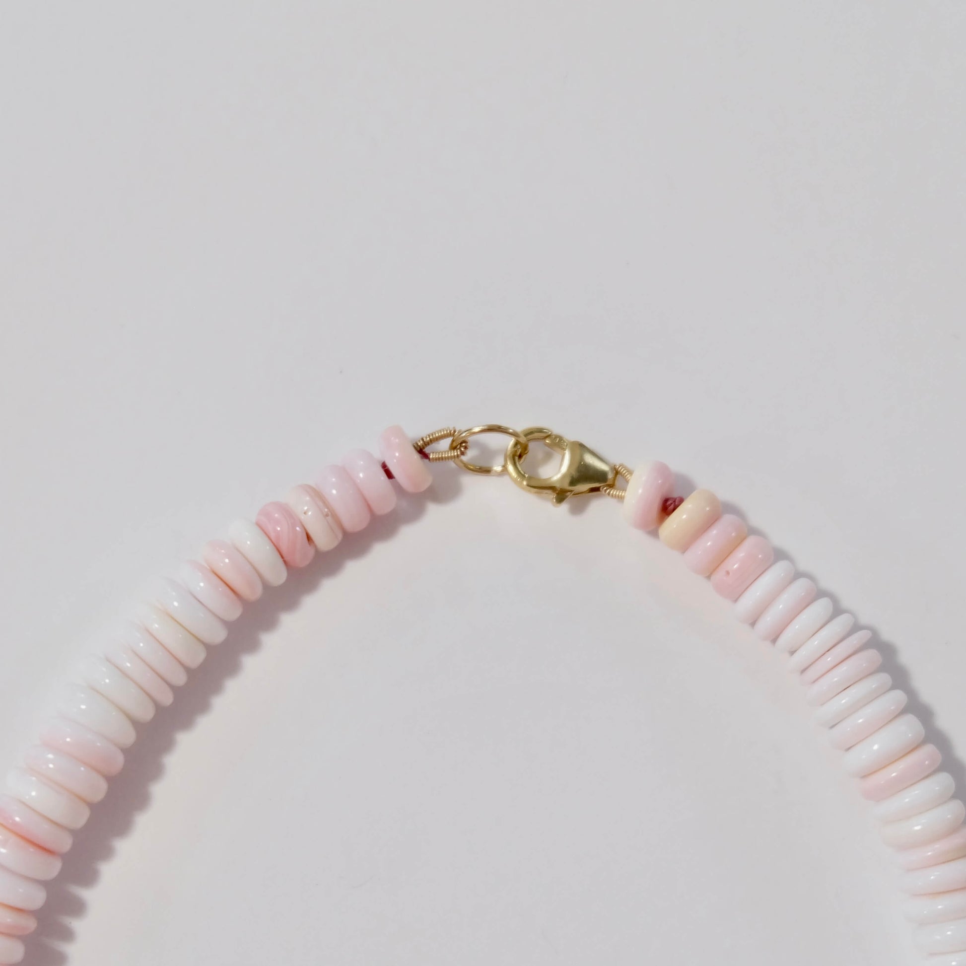 Necklace with pink beads and gold clasp on a light gray background