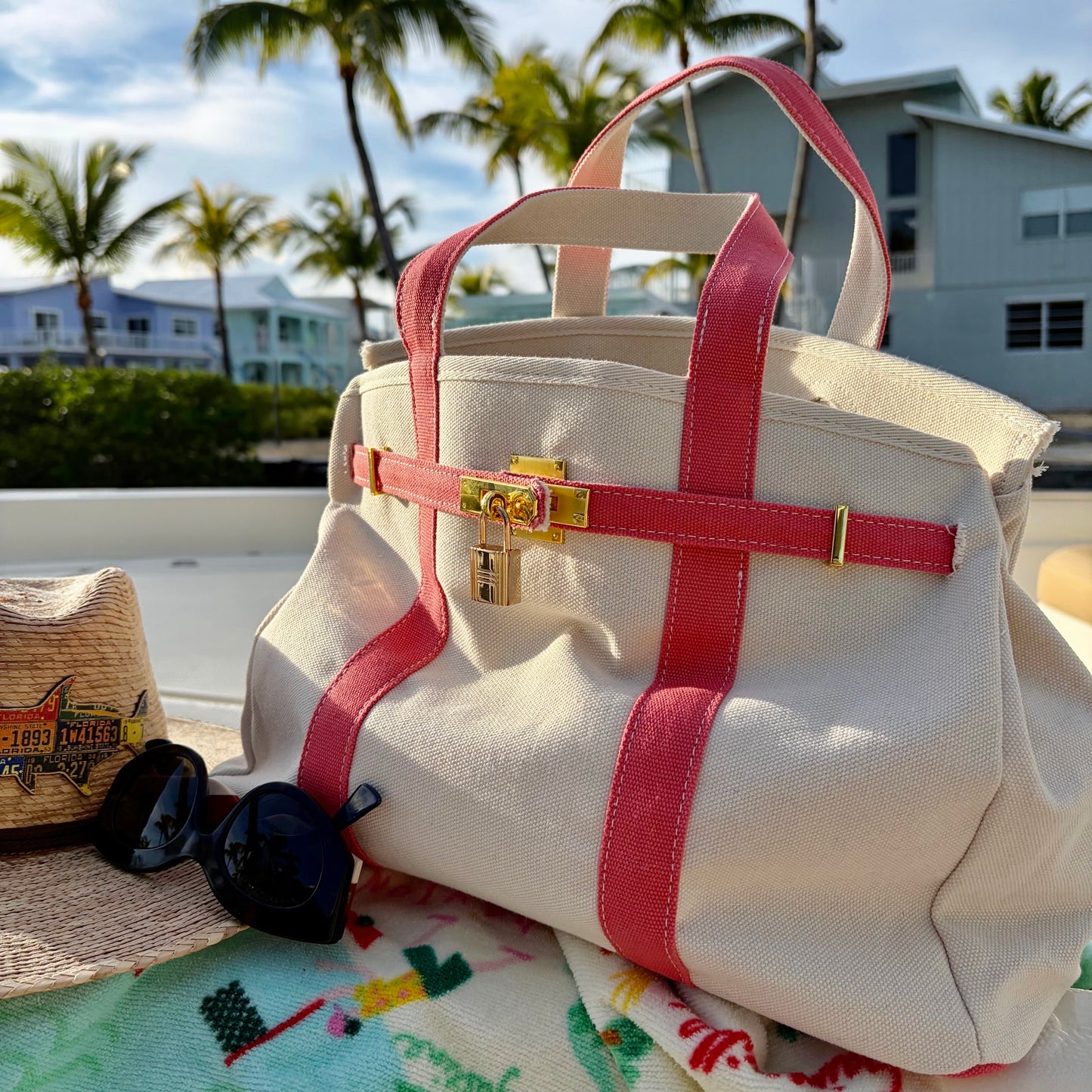 Pink Boatkin tote bag on a colorful surface with palm trees and buildings in the background