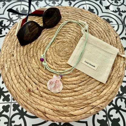 Pink shell pendant with amethyst and rose quartz displayed on woven mat with pouch