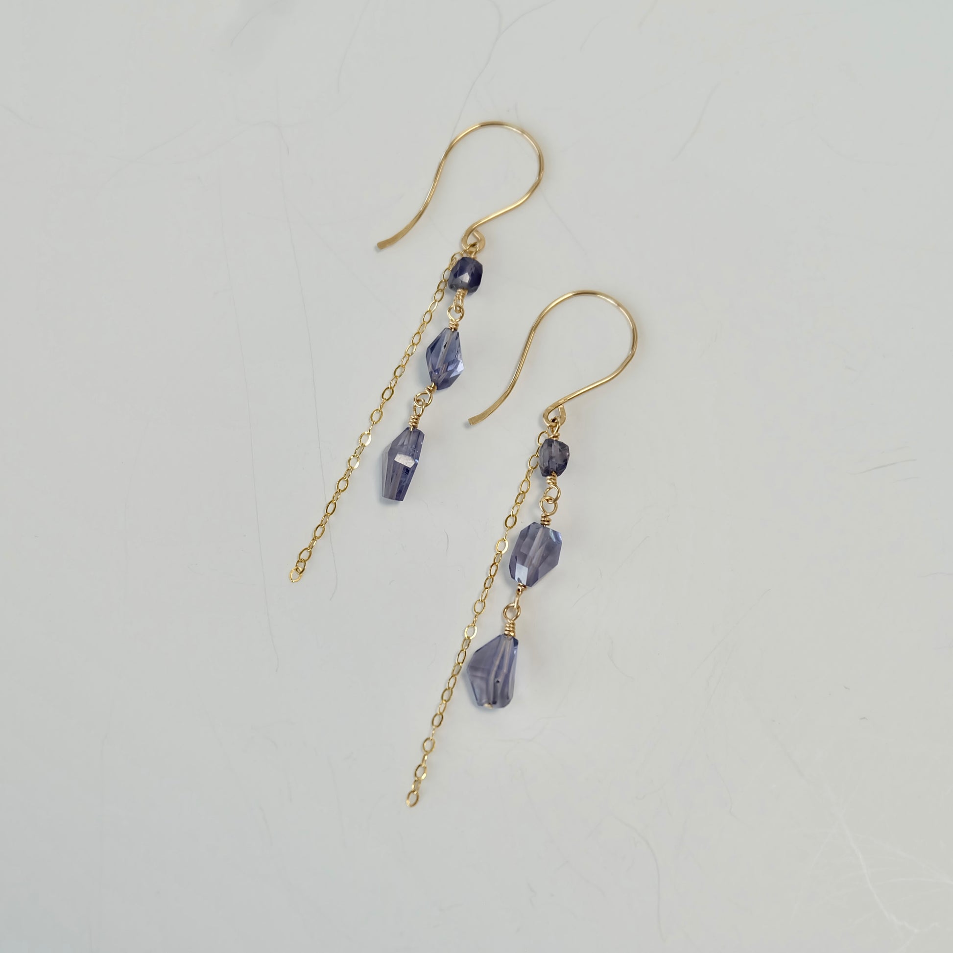 Purple iolite dangle earrings with beads on a light gray background
