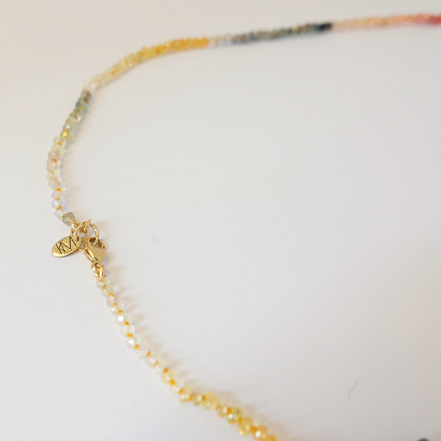 Flat lay of the Rainbow Sapphire Necklace, highlighting its colorful sapphire beads and 14K gold lobster clasp.