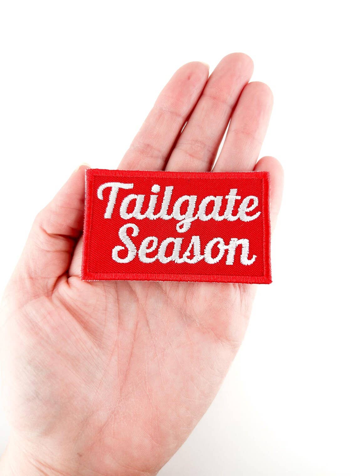 Red patch with 'Tailgate Season' text held in a hand against a white background