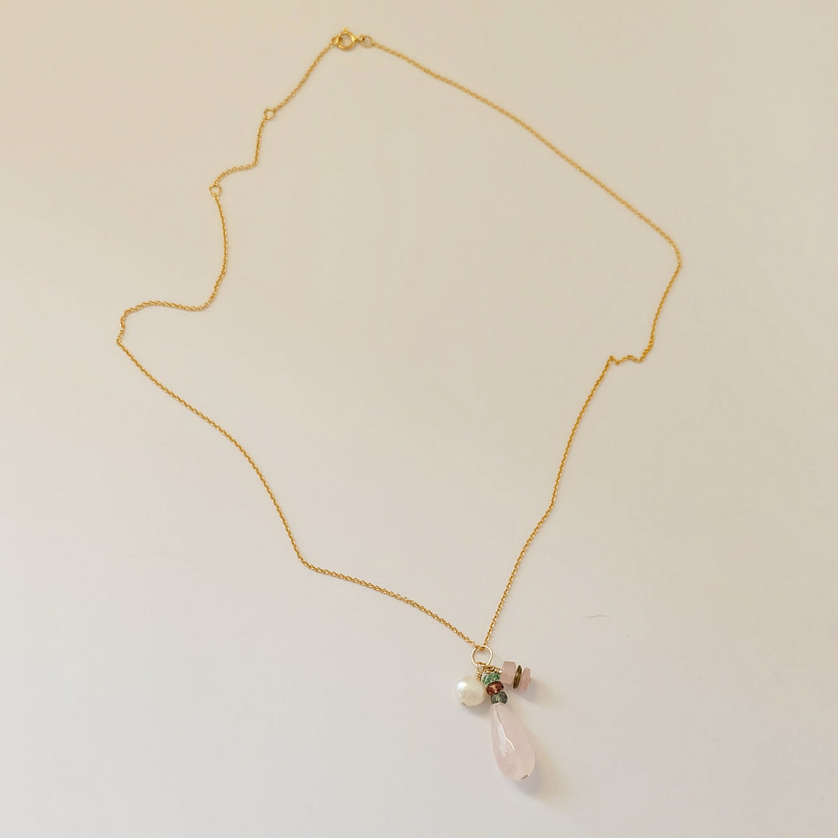 Close-up of rose quartz and tourmaline charms on a dainty gold-filled necklace