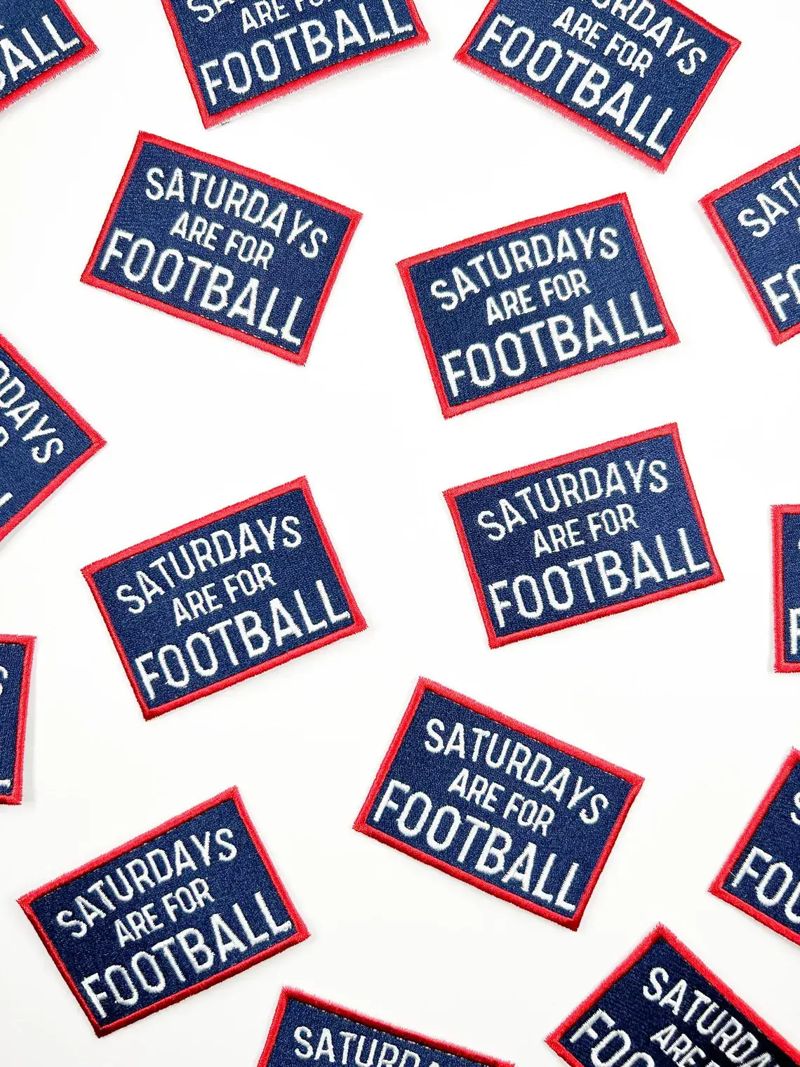Multiple embroidered rectangular patches scattered on a white background, each reading “SATURDAYS ARE FOR FOOTBALL” in white text with a red border and navy blue center.