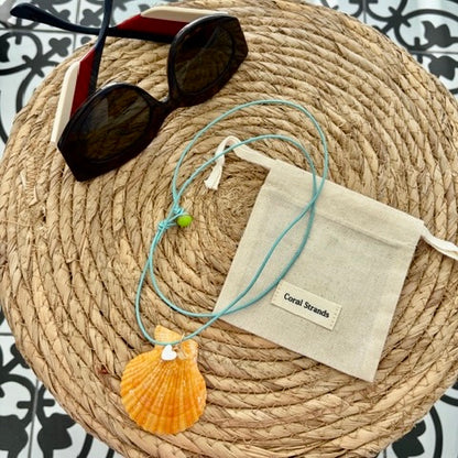 Sea shell pendant necklace with orange shell close-up on woven mat