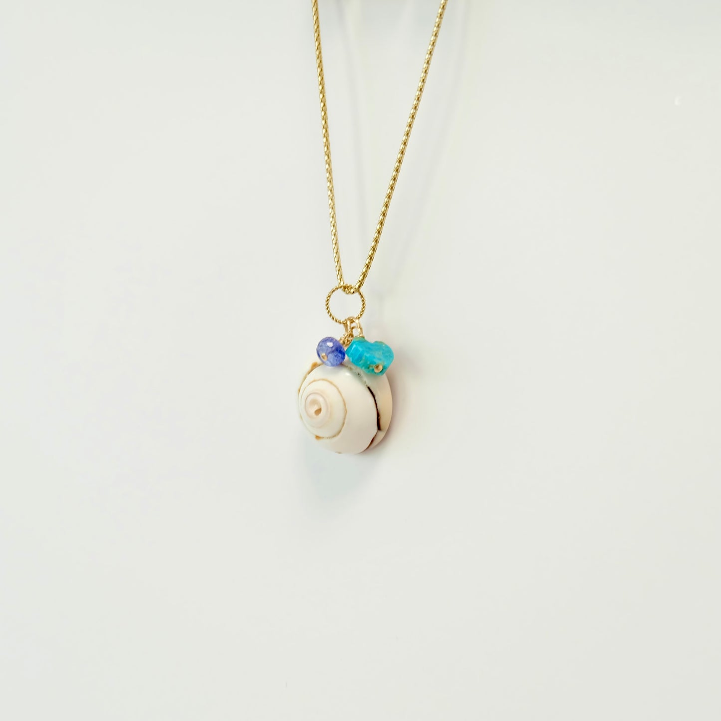 Stunning sea shell charm with turquoise tanzanite and a heart of Kingman turquoise, perfect for beach lovers.