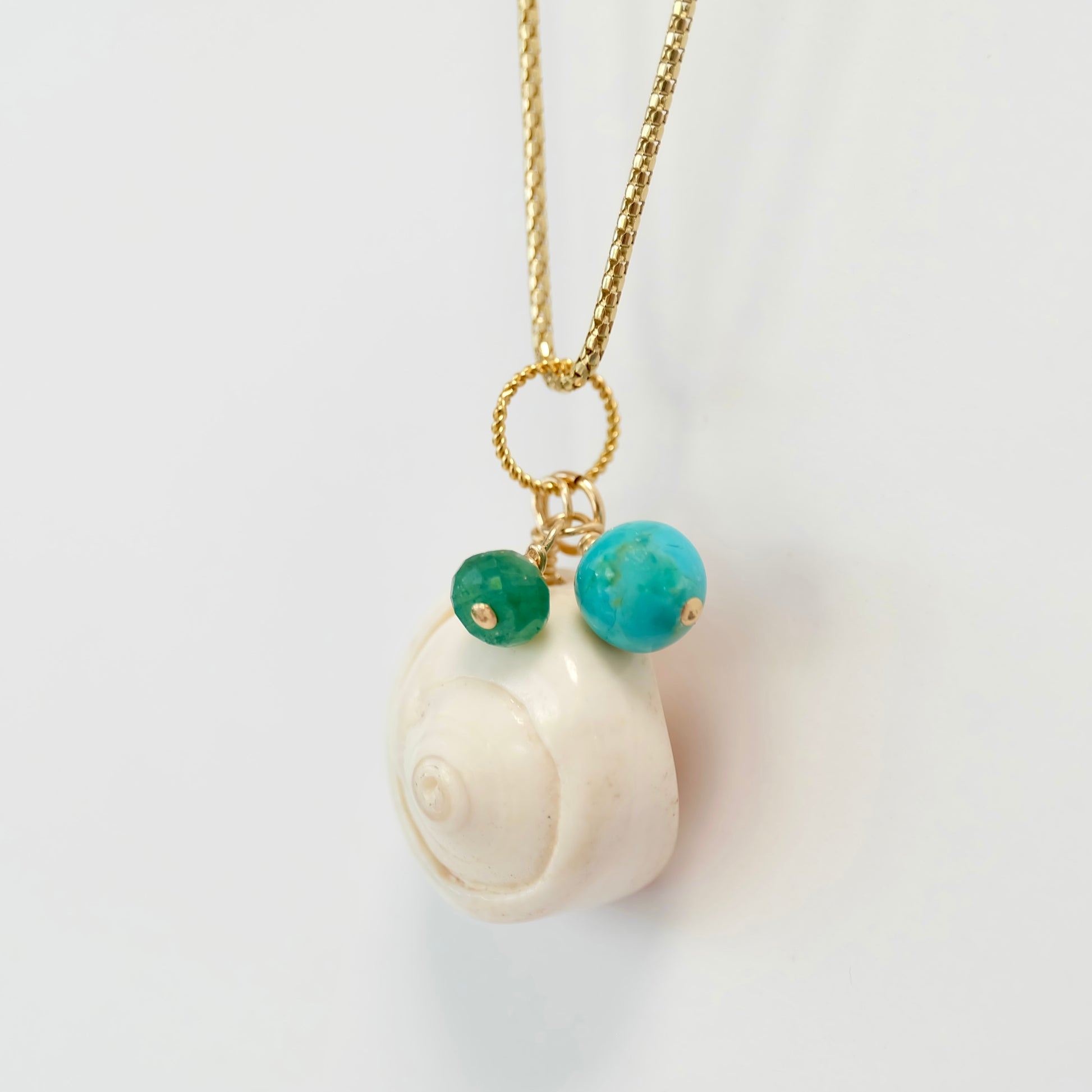 A beautiful turquoise sea shell charm adorned with an emerald, perfect for adding a touch of ocean elegance to any jewelry piece.