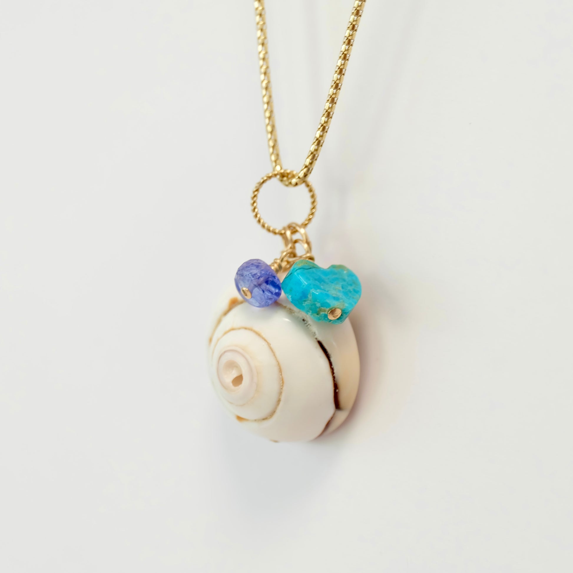 A beautiful sea shell charm featuring a turquoise tanzanite and a heart made of Kingman turquoise.