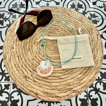 Shell choker with aquamarine beads on turquoise cord, styled on woven mat with pouch and sunglasses