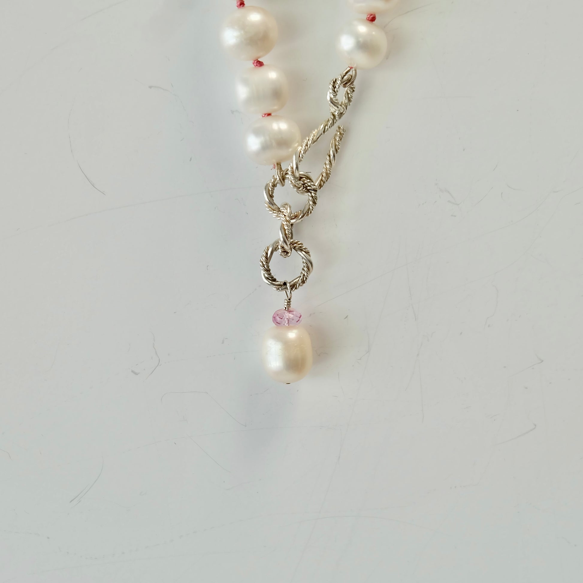 Silver and pearl necklace with pink topaz charm close up on a light gray background