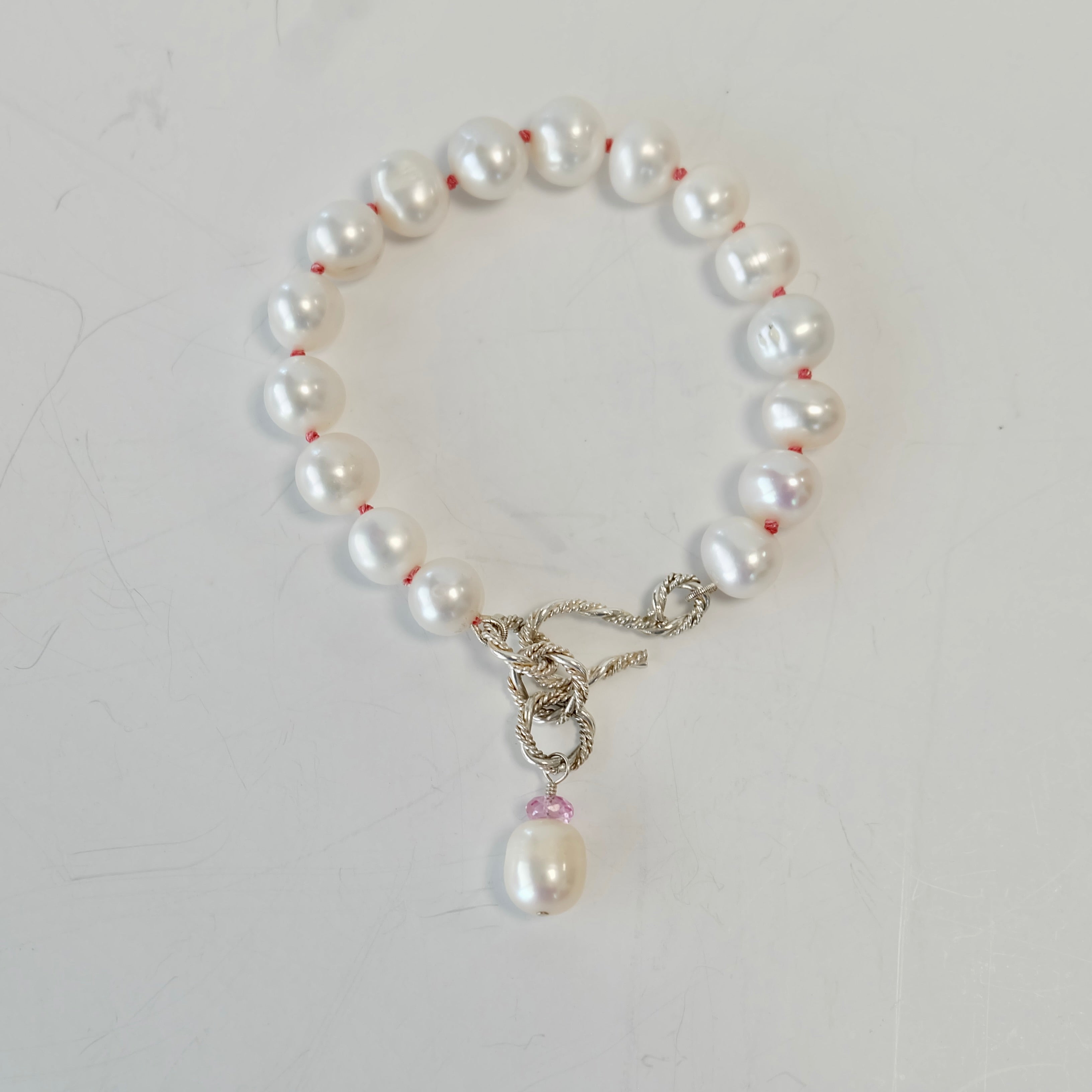 Silver and pearl bracelet with a S clasp and pink accent on a white background