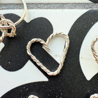 A silver braided heart charm, elegantly designed with intricate detailing, symbolizing love and connection.