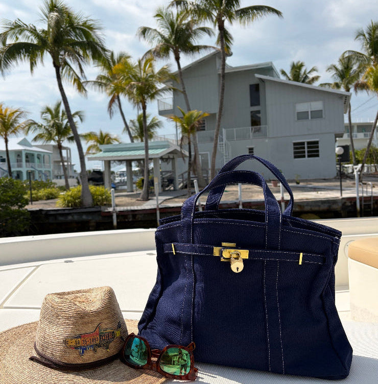 Solid navy Boatkin bag on a boat with palm trees and house in the background