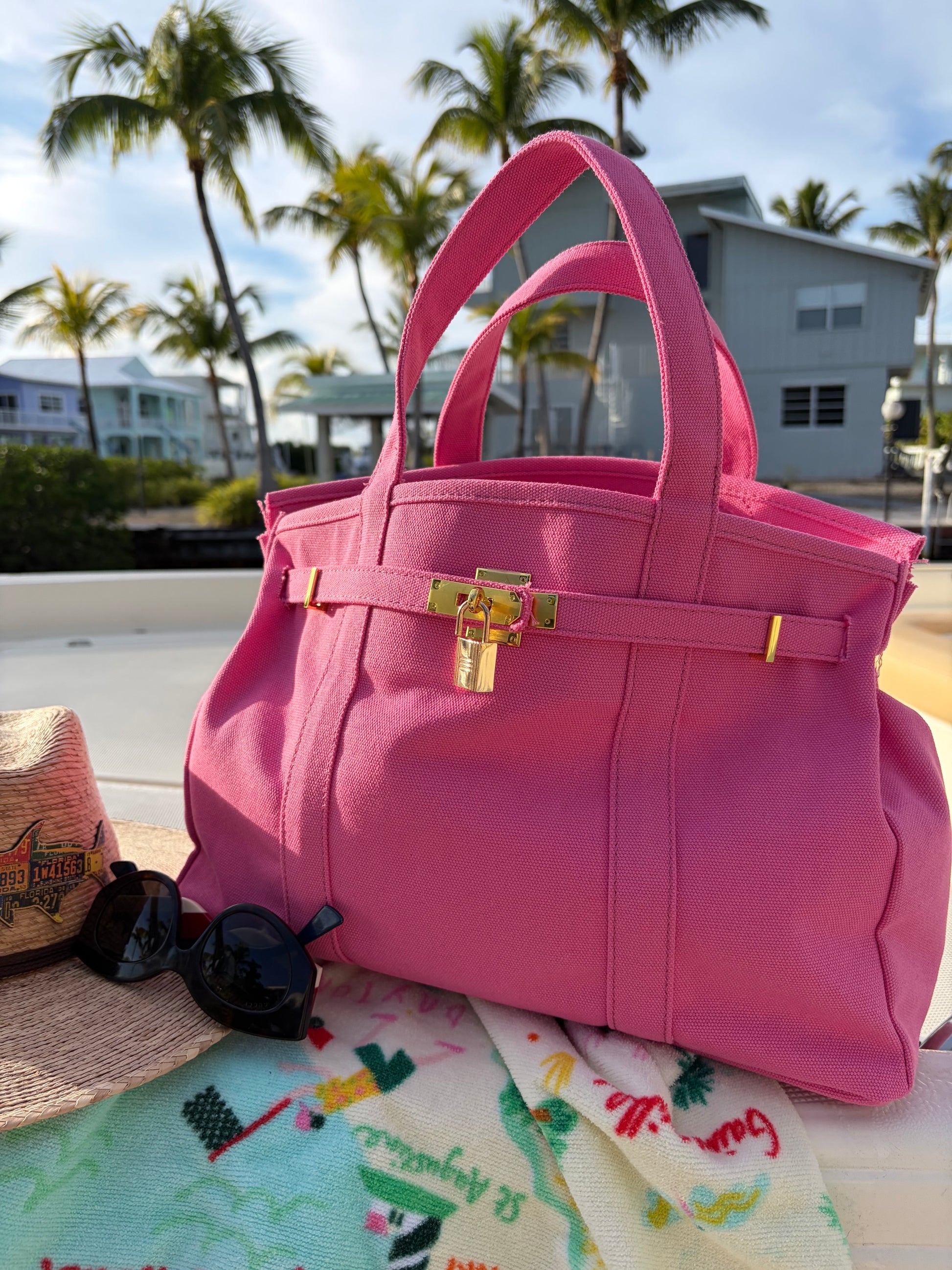 Solid pink Boatkin bag on a boat deck with palm trees and houses in the background.