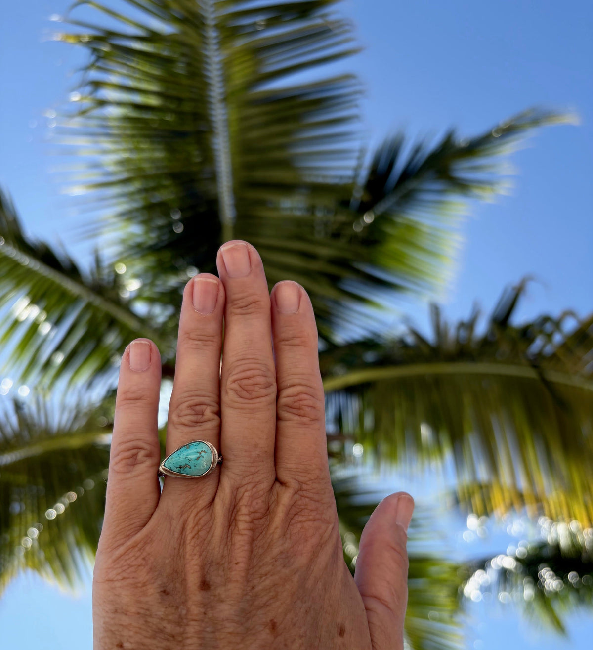 Woman's hand wearing a sterling silver pear shaped turquoise ring