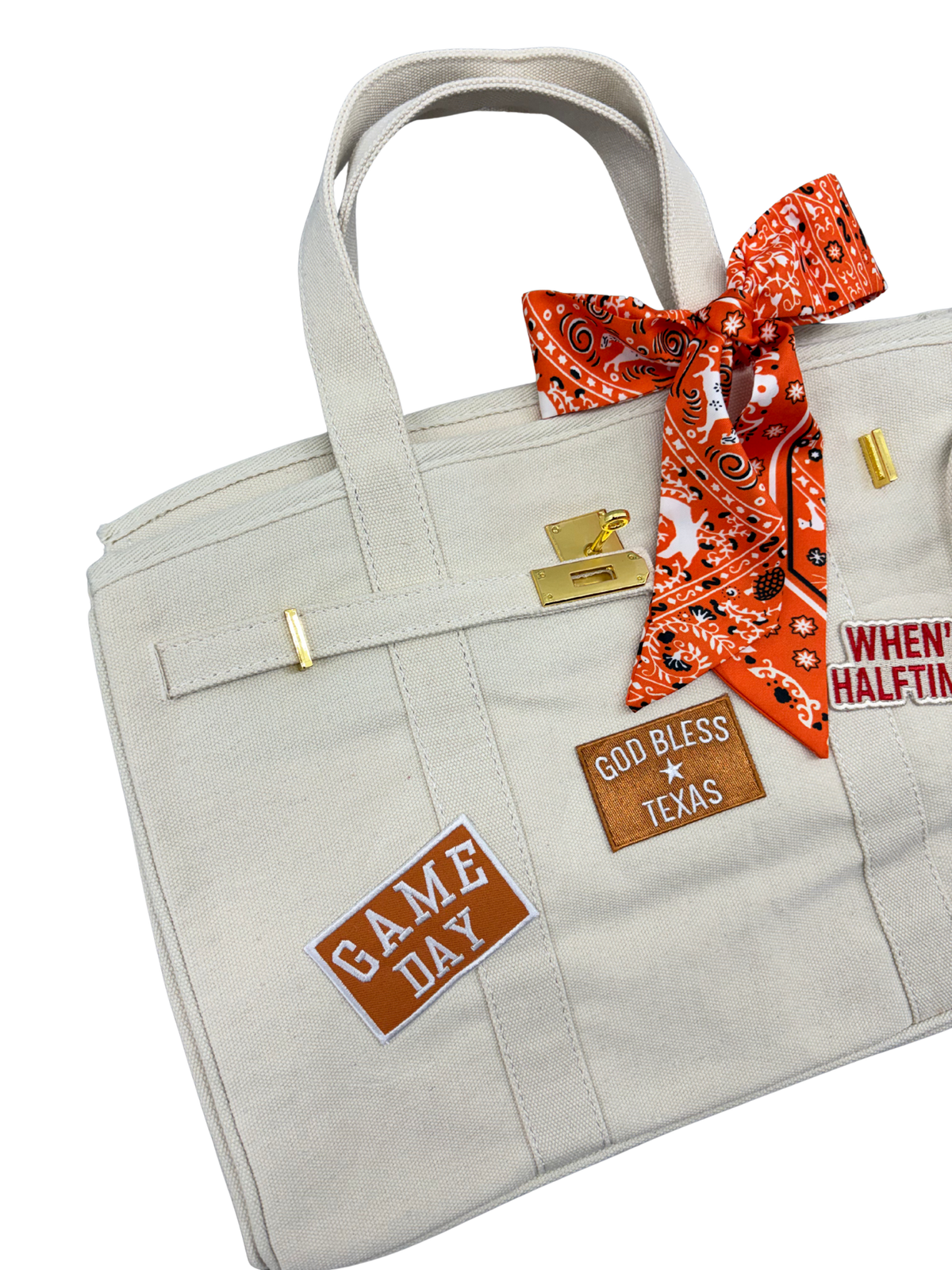 Close up left angle of the cream Texas Longhorns canvas weekender tote bag showcasing an orange and white Game Day patch and a leather God Bless Texas patch with gold hardware.
