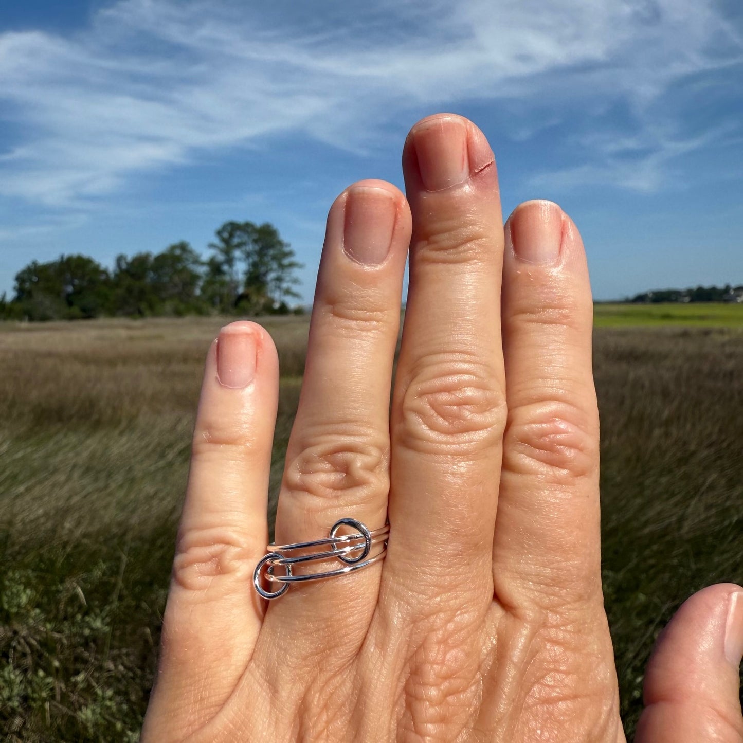 Woman's hand showing a thin interlocking ring in sterling silver.