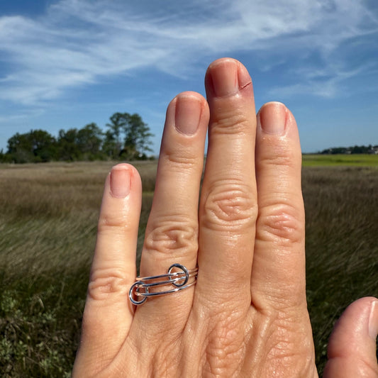 Woman's hand showing a thin interlocking ring in sterling silver.