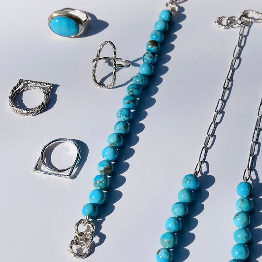 Turquoise beaded bracelet and silver rings on a white background