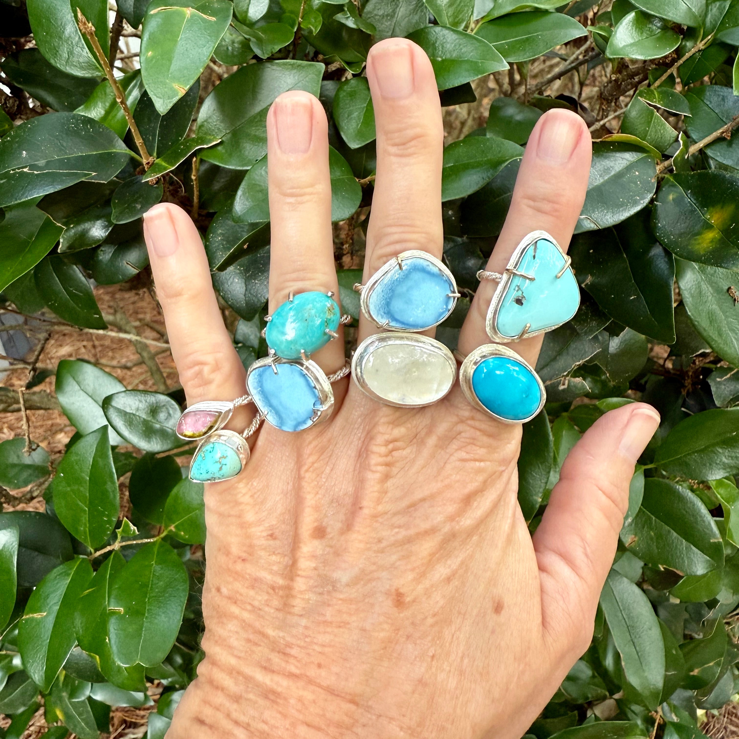 Woman's hand wearing a collection of turquoise rings