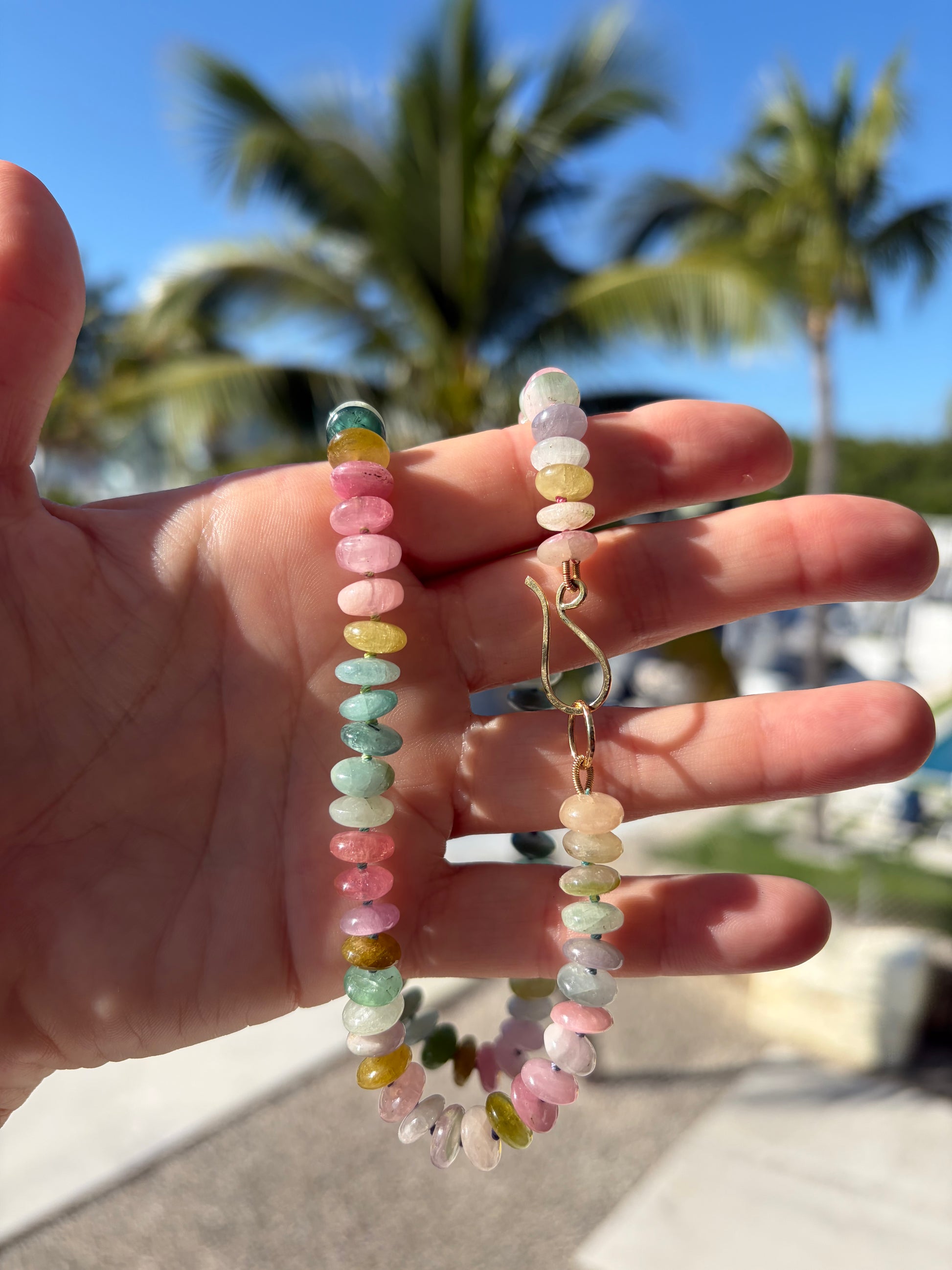 Hand holding two beaded necklaces with a blurred outdoor background