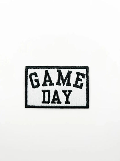 A rectangular embroidered patch with the words 'GAME DAY' in black varsity-style lettering on a white background, outlined with a black border, shown on a plain white surface.