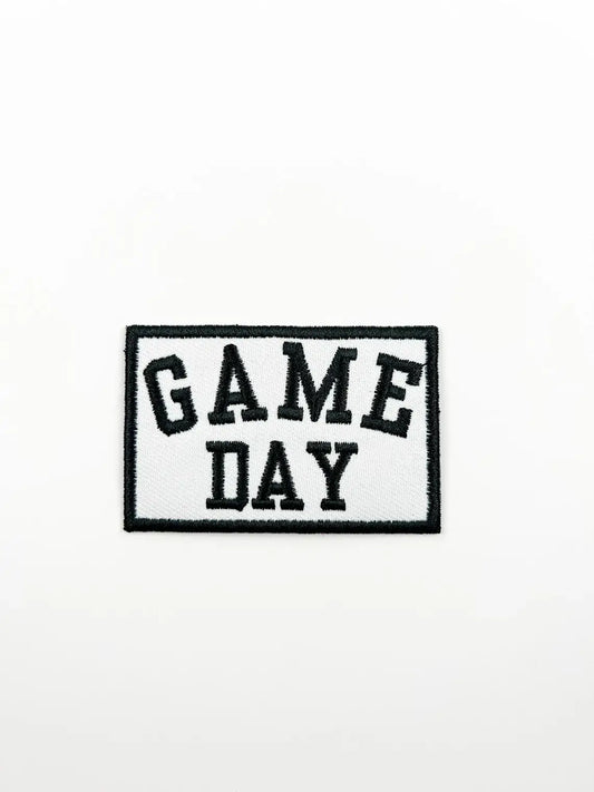A rectangular embroidered patch with the words 'GAME DAY' in black varsity-style lettering on a white background, outlined with a black border, shown on a plain white surface.