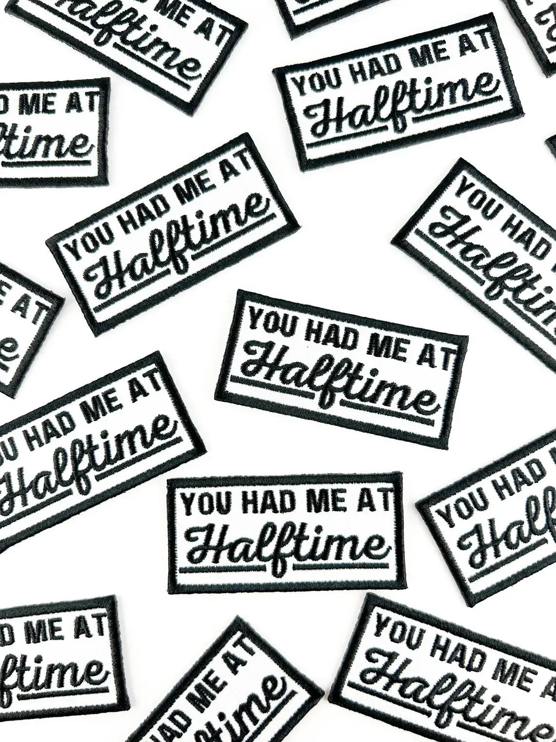 A repeating pattern of rectangular embroidered patches with black borders and white text reading 'YOU HAD ME AT Halftime' on a white background.