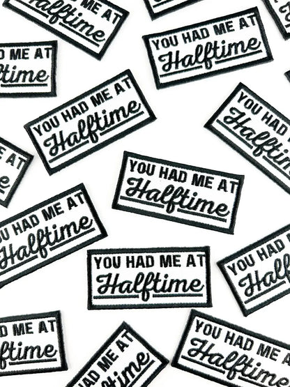 A repeating pattern of rectangular embroidered patches with black borders and white text reading 'YOU HAD ME AT Halftime' on a white background.